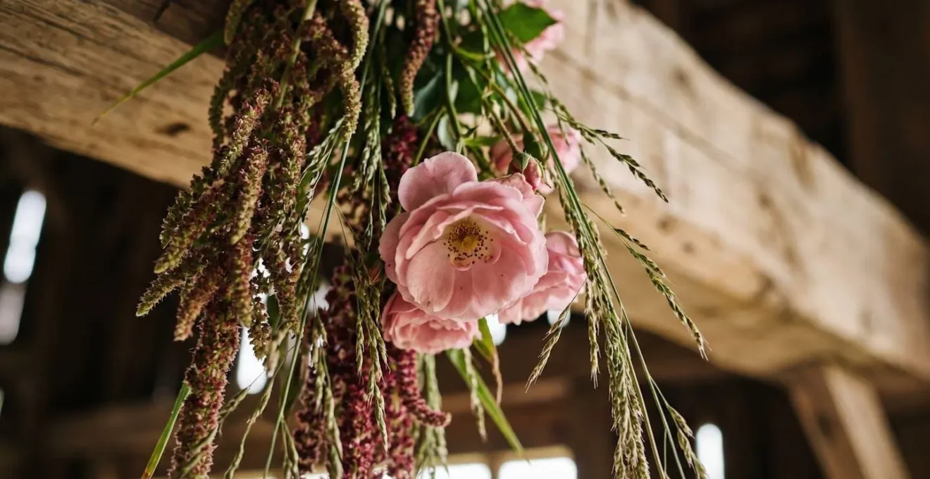 Rustic barn wedding with cascading floral installation hanging from wooden beams viewed from guest perspective below