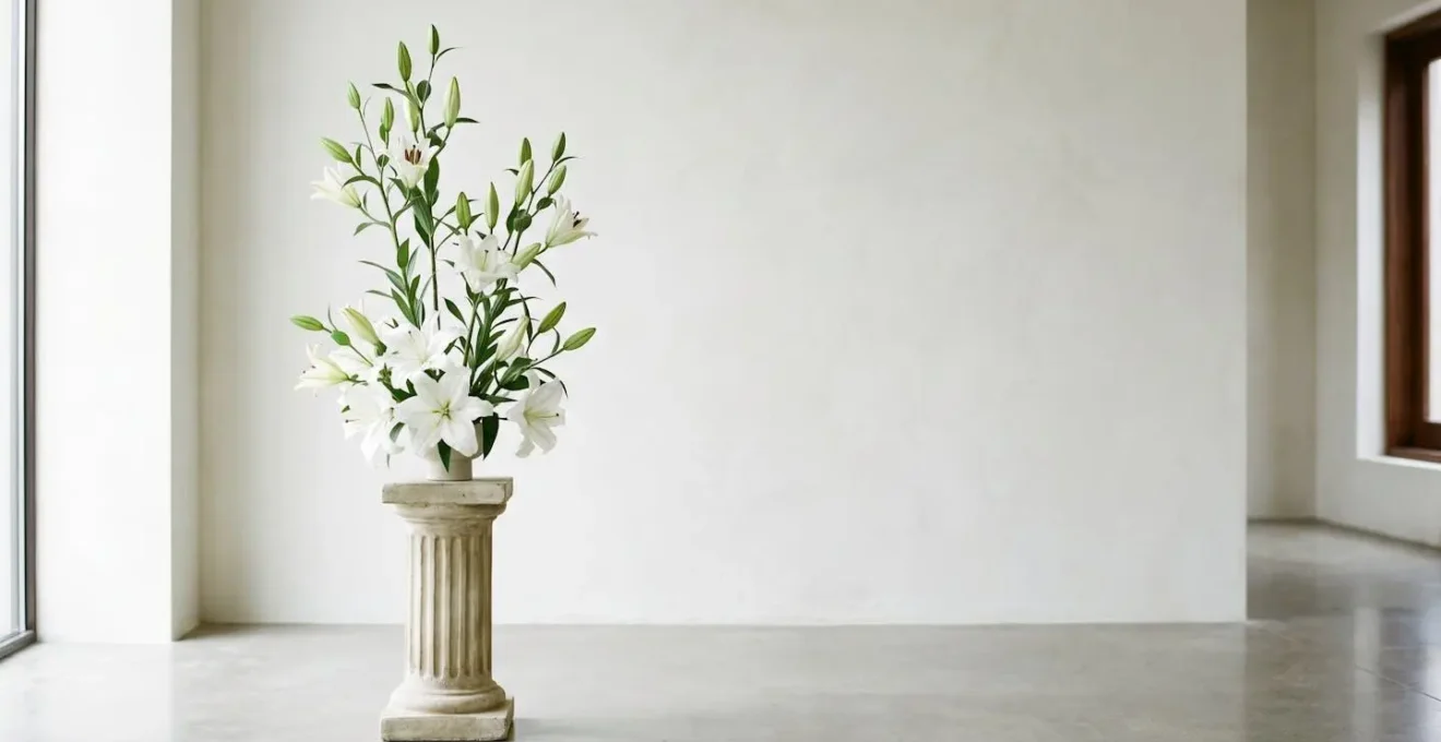 Wide view of an elegant tall lily arrangement on a pedestal, showing vertical line design with blooms at varying heights against a clean minimal background