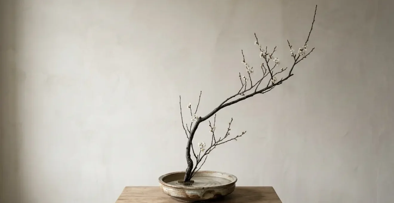 Minimalist Japanese ikebana flower arrangement with asymmetrical branch in ceramic vase on tranquil surface