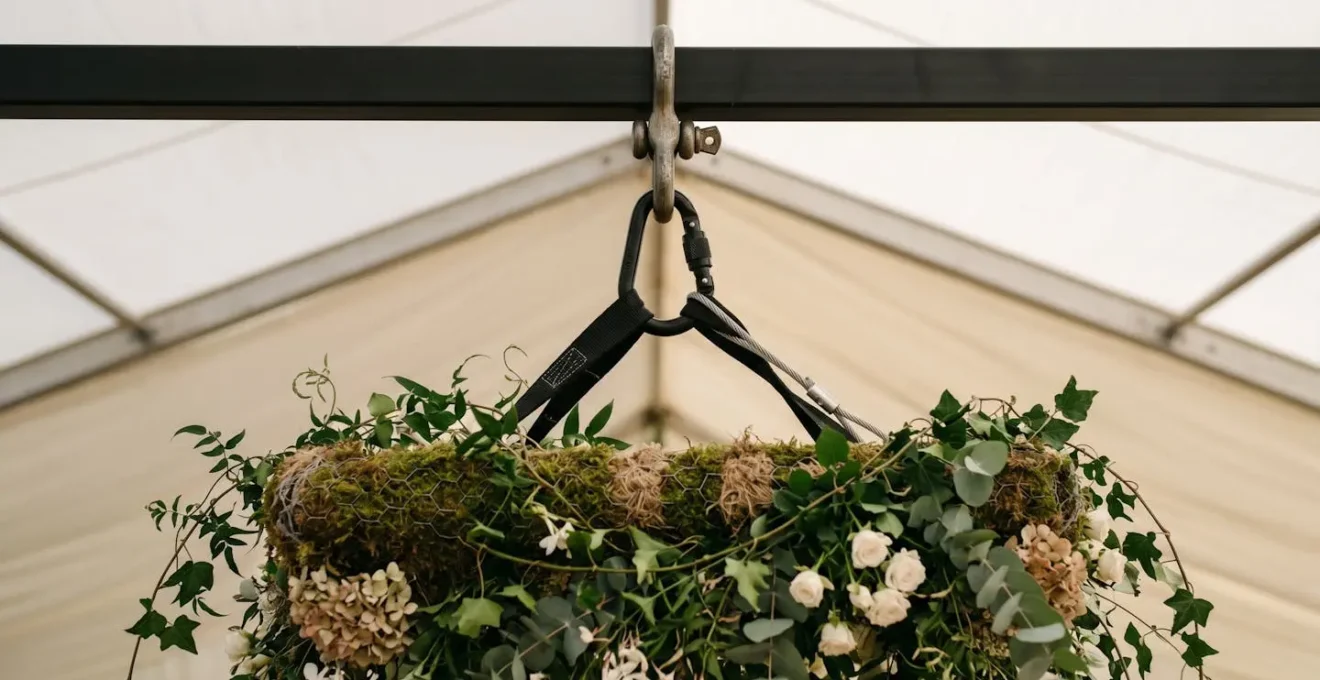 Close-up of professional rigging point with steel cable and safety harness supporting suspended floral installation in UK marquee